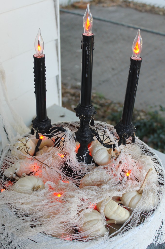 Some small white pumpkins act as filler to hide power cords and white gauze mutes the bright orange holiday string lights.