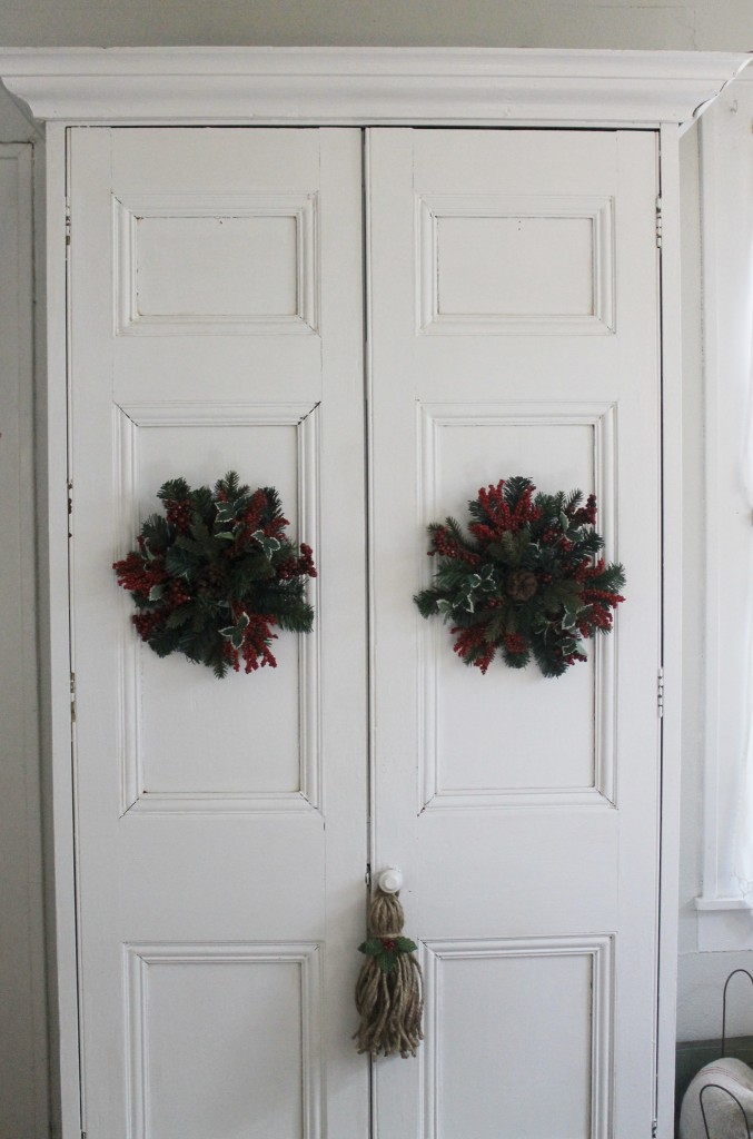 Old houses have many armoires for storage.  Simple white adorned with  wreaths and a hand-made twine tassel with holiday embellishment.