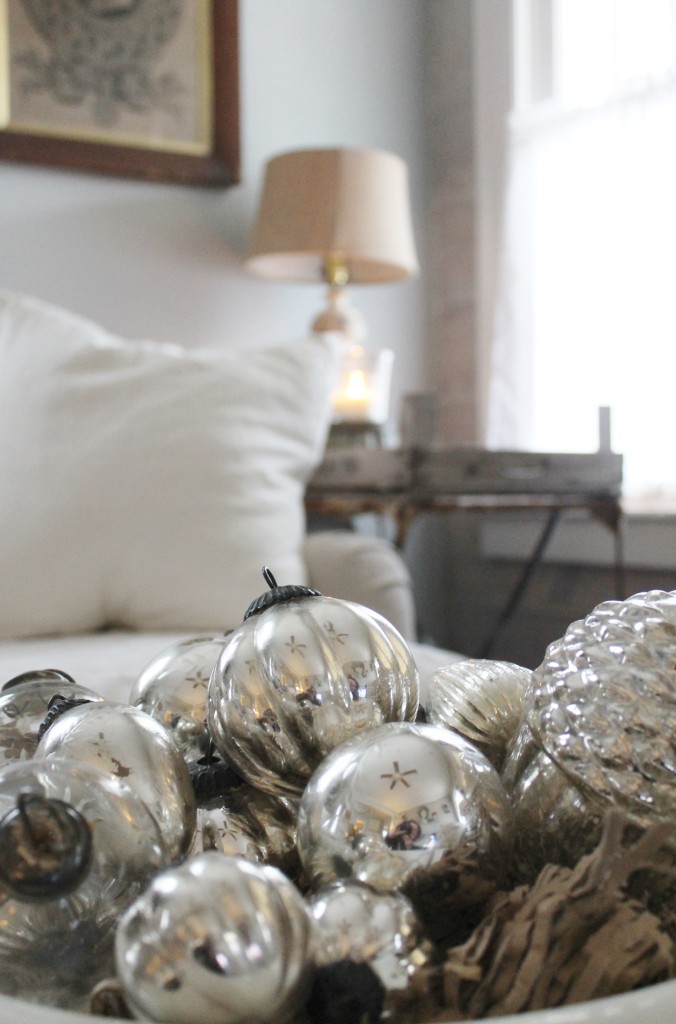 Mercury glass globes in an old ironstone bowl with linen slipcovers in the background.